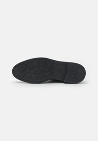 Suela de zapato de goma negra con patrón texturizado, con un diseño plano y logotipo de marca. Superficie antideslizante con varios diseños de banda de rodadura.