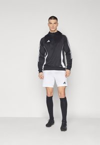 Svart treningshette med hvite detaljer, kombinert med hvite shorts. Sorte knelange sokker og svarte fotballsko fullfører antrekket.