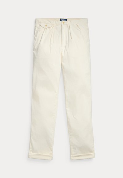 Pantalones de corduroy color crema con pinzas, bolsillos laterales, bolsillo trasero con tapeta abotonada y dobladillos con puños, exhibidos sobre un fondo blanco.