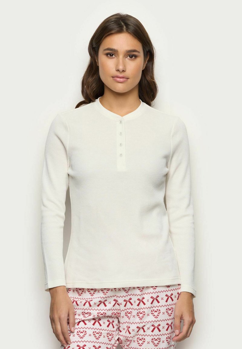 Maglietta henley bianca a maniche lunghe con texture a costine e scollo rotondo, caratterizzata da una fila di quattro bottoni.