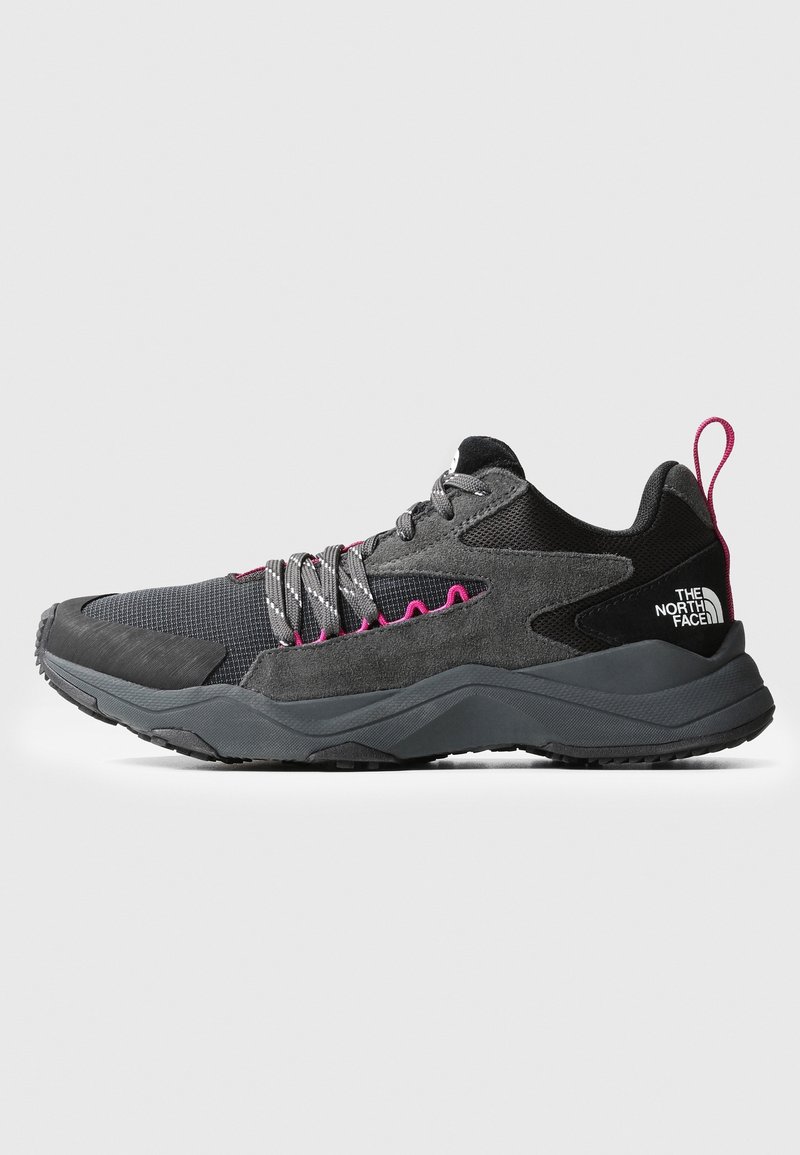 Zapatilla de perfil bajo negra y gris con acentos en rosa, cordones con diseño y el logo de The North Face en el talón, mostrada en vista lateral.