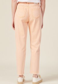 Pantalones vaqueros de mezclilla melocotón con un corte recto, que presentan dos bolsillos traseros y costuras visibles. Combinados con calzado claro.