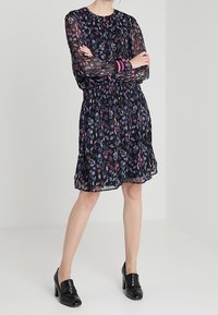 Svart blommig klänning med långa genomskinliga ärmar, åtsittande midja och flerlagad kjol. Har texturerade blomster mönster i nyanser av lila och rosa.