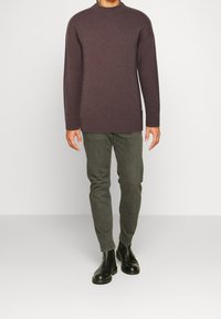 Brauner, gerippter Strickpullover mit hohen Kragen, kombiniert mit grauen Slim-Fit-Hosen und schwarzen Ankle Boots. Einfaches Design, keine sichtbaren Muster.