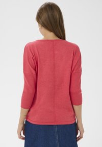 Pull tricot corail à manches trois-quarts, avec poignets et ourlet côtelés, présentant une couture centrale dans le dos pour plus de détails.