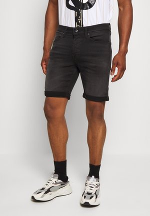 Shorts de mezclilla negra con dobladillos enrollados, que presentan un corte ajustado y un desvanecimiento sutil. Llevados con una camiseta gráfica blanca y zapatillas deportivas.