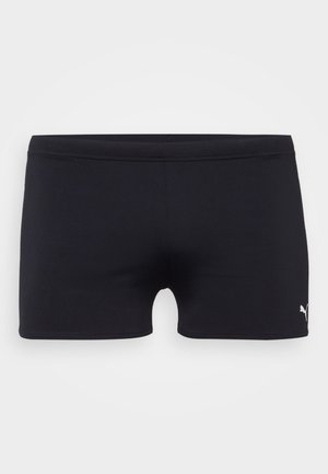 Schwarze sportliche Shorts aus dehnbarem Material, mit einem niedrig geschnittenen Design und einem kleinen weißen Logo auf der unteren rechten Seite.