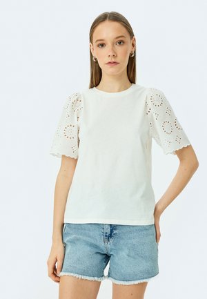 Witte T-shirt met korte, geborduurde mouwen met scalloped randen en bloemen uitsnijdingen, gecombineerd met denim shorts. Glad katoentextuur.