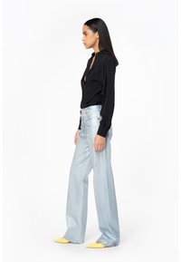 Camicia nera con bottoni abbinata a jeans a gamba larga azzurri a vita alta e mule gialli, con una texture morbida e una finitura lucida.