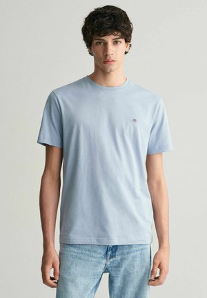 Světle modré bavlněné tričko s kulatým výstřihem, krátkými rukávy a malým vyšitým logem na hrudi. Klasický střih s hladkou текстurou.