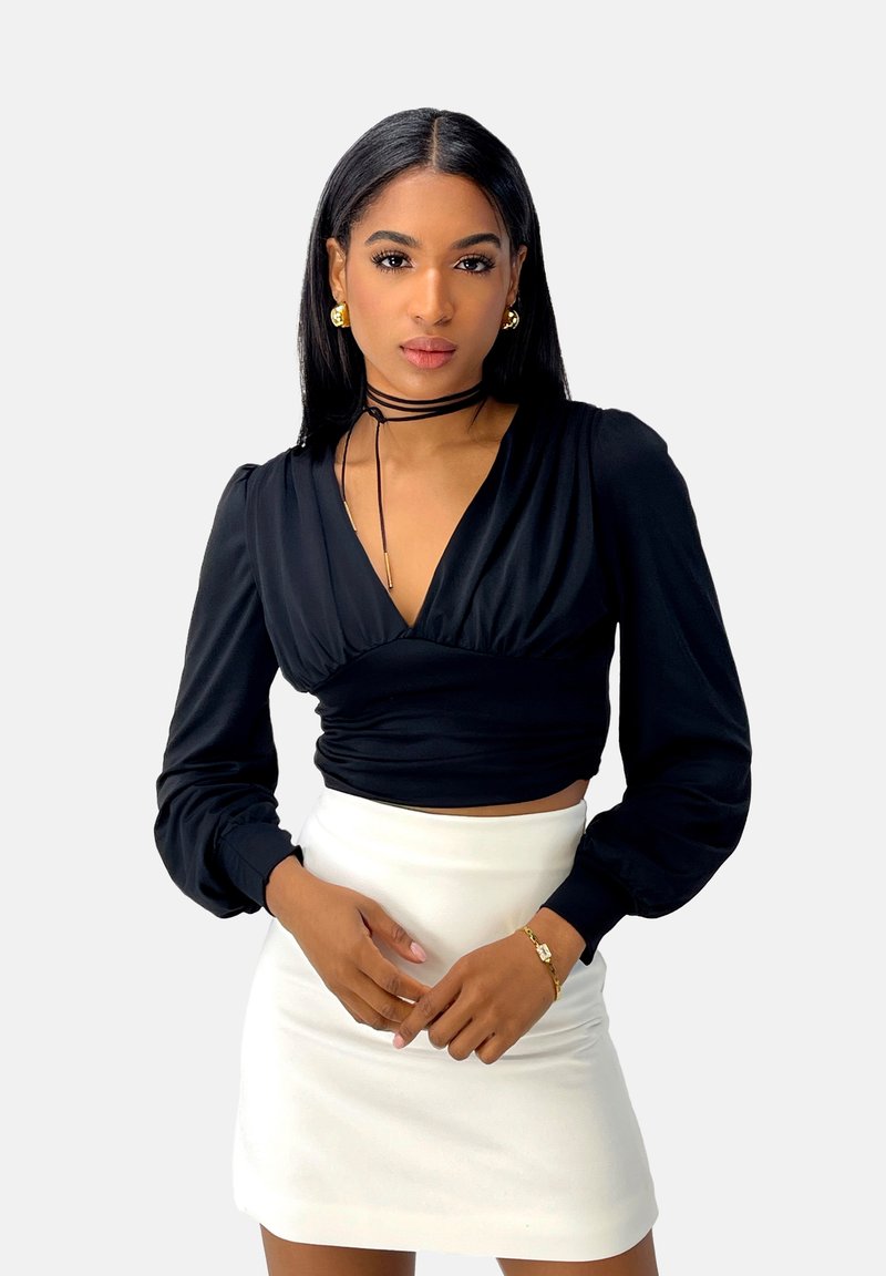 Zwart wikkelshirt met lange mouwen en opgeblazen mouwen, gedragen met een witte minirok. Heeft een diepe halslijn en een zwarte choker als accessoire.