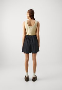 Débardeur jaune tricoté avec des bords ondulés, associé à un short noir doté d'une taille élastique et d'une coupe décontractée, porté avec des chaussures marron.