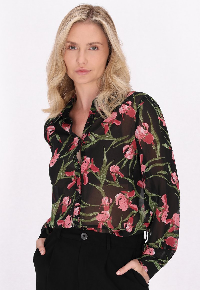 Bluză neagră transparentă cu un imprimeu floral ce prezintă flori roz și frunze verzi, cu mâneci lungi și închidere cu nasturi. Asortată cu pantaloni negri.