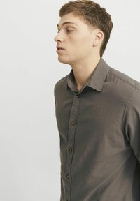 Camisa de botones en tela gris oscuro, con un cuello clásico, botones frontales y una textura suave. Modelo mostrado en perfil lateral.