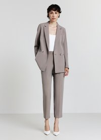 Hellgrauer maßgeschneiderter Anzug mit doppelreihigem Blazer und geraden Hosen, kombiniert mit einem weißen Top und spitzen weißen Pumps.