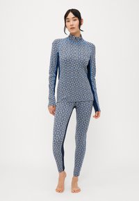 Långärmad blå mönstrad surfdräkt med hög krage, med ett geometriskt mönster och enfärgade accenter på sidorna.