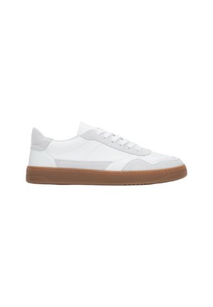White leather sneakers with grey suede accents, round toe, flat laces, and a textured brown rubber sole. Minimalistic design elements.
