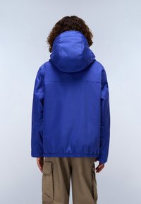 Modrá kapuce bunda vyrobená z voděodolného materiálu, s elastickým lemem, rovného střihu a bočními kapsami, nošená přes béžové cargo kalhoty.