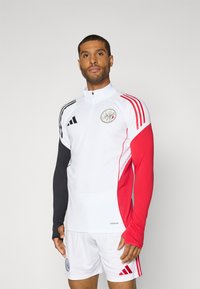Hvid atletisk skjorte med sorte og røde ærmer, med en halvmatchende krave og logo. Akkompagneret af hvide shorts med røde detaljer.