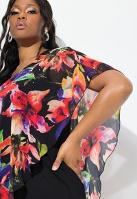 Blumenleiter Poncho in Schwarz, mit lebhaften roten, orangefarbenen und grünen Blumen. Weicher, fließender Stoff mit lockerer Passform und geschwungenen Kanten.