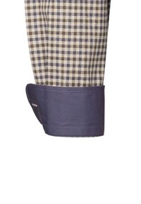 Polsino di camicia a quadretti con quadrati beige e marroni, con un bordo di colore blu scuro solido, che mostra una texture di tessuto liscia.