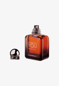Vierkante glazen parfumfles met een donkere amberkleur, zilveren hardware en een ronde zwarte dop, gelabeld "Stronger with You Absolutely."