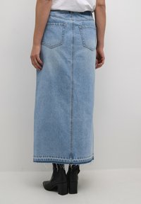 Maxi-Jeansrock in Hellblau, mit geradem Schnitt, Gesäßtaschen und rohem Saum. Getragen mit schwarzen Ankle Boots.