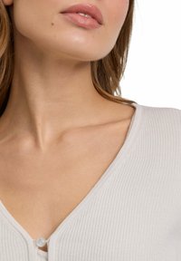 Hellgrau gerippter Top mit V-Ausschnitt und einem kleinen Perlenknopfdetail in der Mitte. Glatte Textur mit engem Sitz.