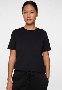 Musta puuvillapaita, jossa on pyöreä kaula-aukko ja lyhyet hihat. Yksinkertainen muotoilu, pehmeä pinta ja rento istuvuus. Minimimerkintä näkyvissä.