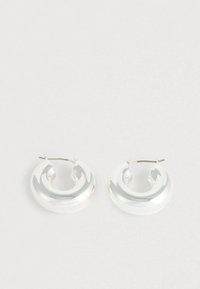 Okrugle naušnice u boji srebra s glatkim, zaobljenim dizajnom. Izrađene od reflektirajućeg materijala, s diskretnim zakrivljenim oblikom i metalnim zatvaračem.
