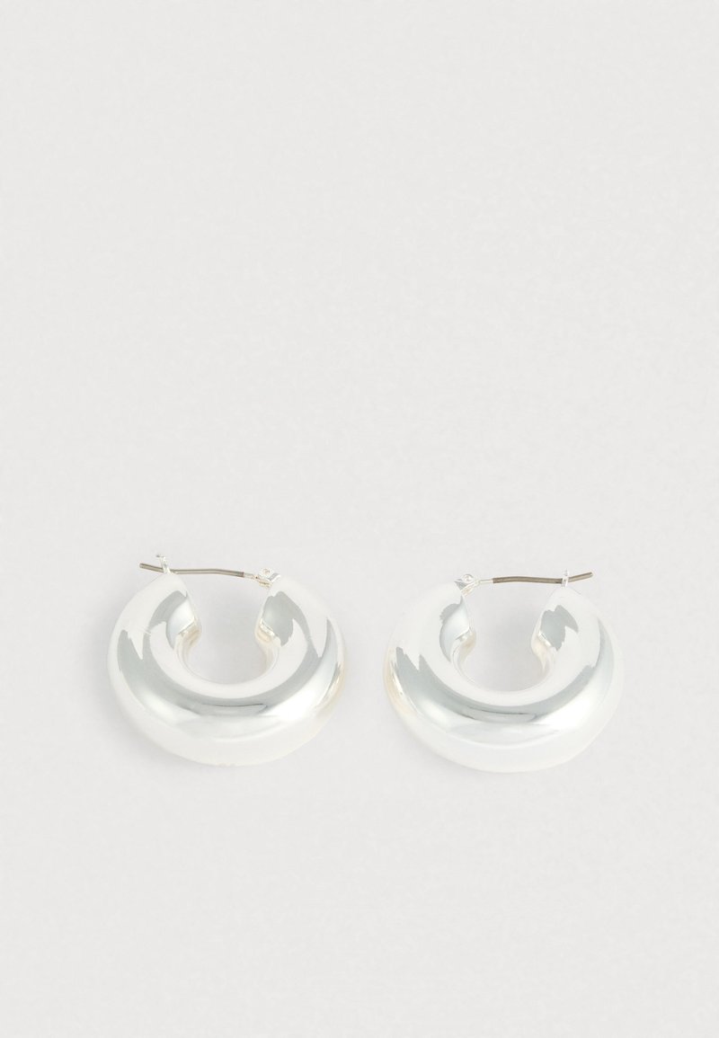 Okrugle naušnice u boji srebra s glatkim, zaobljenim dizajnom. Izrađene od reflektirajućeg materijala, s diskretnim zakrivljenim oblikom i metalnim zatvaračem.