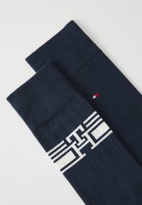 Chaussettes côtelées navy avec un logo et des rayures blanches en haut. Présente un petit accent rouge, blanc et bleu sur le côté. Texture de matériau douce.