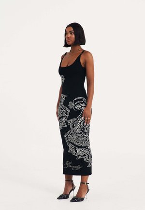 Long black dress with white graphic designs, made of a smooth material. Features a scoop neckline and fitted silhouette. Paired with black heels.