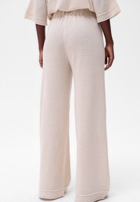 Pantalons larges beige en tissu texturé avec une taille élastique, présentant un ourlet plat et une coupe ample pour plus de confort.
