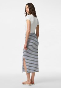 Jupe maxi rayée avec fente latérale, présentant des rayures bleues, blanches et brunes. Assortie à un haut blanc ajusté et des tongs.