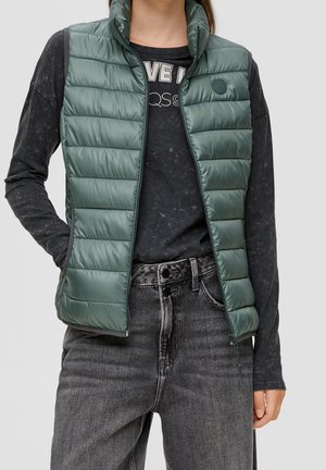 Groene puffer vest met hoge kraag en ritssluiting, met een horizontaal geborduurd ontwerp. G gedragen over een zwart shirt met lange mouwen en grijze jeans.
