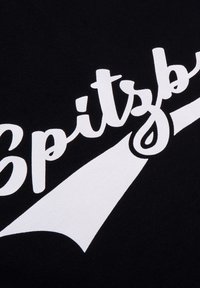 Zwarte stof met grote, witte gestileerde tekst die "Spitzb." vormt. Een witte grafische afbeelding strekt zich uit vanaf de tekst, wat een dynamisch visueel effect creëert.