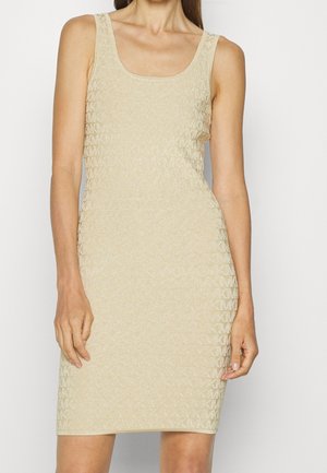 Robe beige sans manches longueur genou avec un motif texturé subtil portée par une personne devant un fond clair uni.