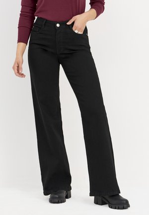 Zwarte wijde jeans gemaakt van denim, voorzien van een knoopsluiting, frontzakken en een hoge taille. Gecombineerd met zwarte plateau laarzen.