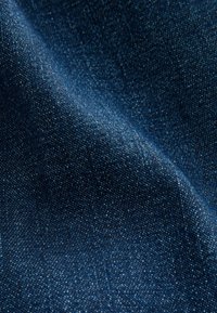 Mørkeblå denimstof med en let glans, der har en glat tekstur og et subtilt kornmønster, vist i en krøllet position.
