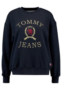 Mörkblå sweatshirt med "TOMMY JEANS"-logotyp i guld, med en broderad sköld med ett lejon, ribbade ärmslut och nederkant. Mjuk fabriksstruktur.