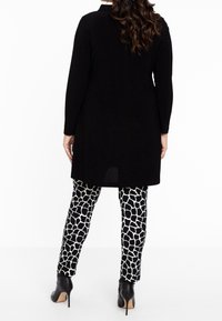 Schwarzes Langarm-Tunica-Oberteil kombiniert mit Leggings im Schwarz-Weiß-Giraffenmuster, mit einem eleganten Design und schwarzen High-Heels.