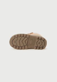 Une seule chaussure en caoutchouc brun vue du dessous, avec le motif de la semelle et la marque de taille 26 visibles sur un fond uni.
