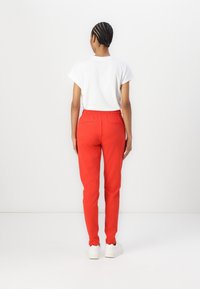 Röda joggers med elastisk midja, bakfickor och smalnande ben, kombinerade med en enkel vit T-shirt med kort ärm och vita skor.