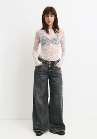 Csipkés body hosszú ujjakkal egy szürke bralette fölött, magas derekú, bő szárú fekete farmernadrággal párosítva. Fekete slip-on cipők.