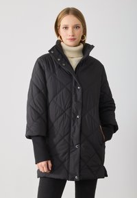 Schwarze gesteppte Puffjacke mit Druckknöpfen, hohem Kragen und gerippten Ärmelbündchen. Sie hat eine lockere Passform und zwei Seitentaschen.