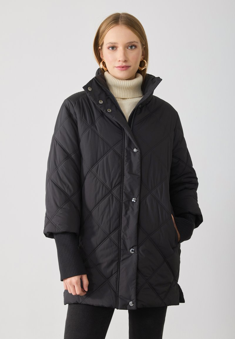 Schwarze gesteppte Puffjacke mit Druckknöpfen, hohem Kragen und gerippten Ärmelbündchen. Sie hat eine lockere Passform und zwei Seitentaschen.