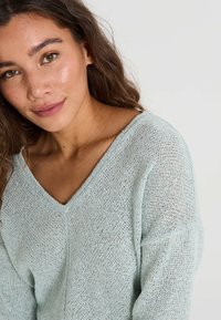 Suéter de punto azul claro con diseño de escote en V, que presenta un corte holgado y un patrón texturizado, destacando la tela transpirable.