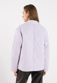 Lavendel, kviltet jakke med krage, med et teksturert mønster og rett snitt, båret med blanke svarte bukser.