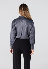 Grijze satijnen shirt met lange mouwen, rug yoke detail, en knoopsmanchetten, gecombineerd met zwarte broeken. Gladde textuur en losse pasvorm.